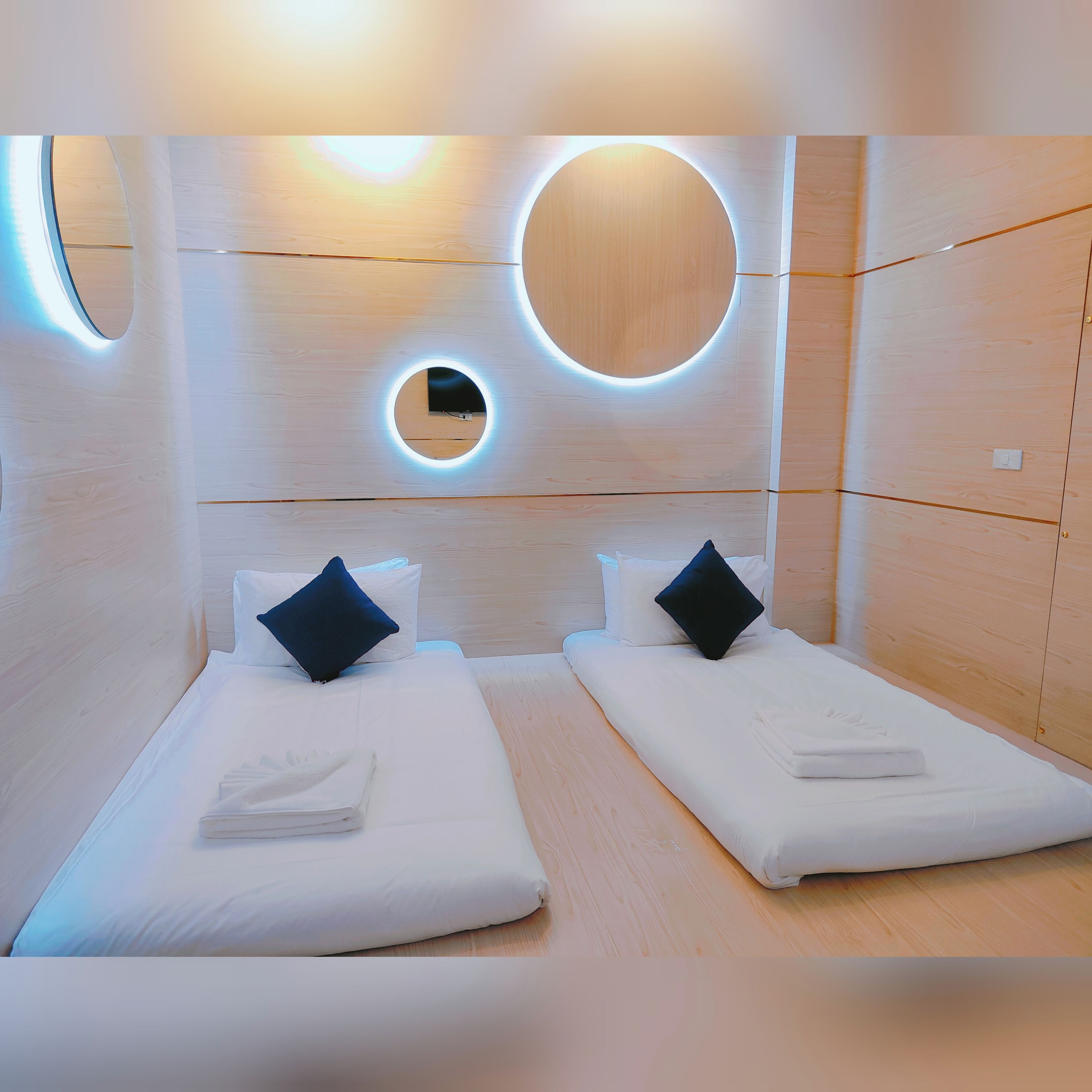 Una habitación de hotel moderna con dos camas, un espejo circular y un diseño de pared de madera.
