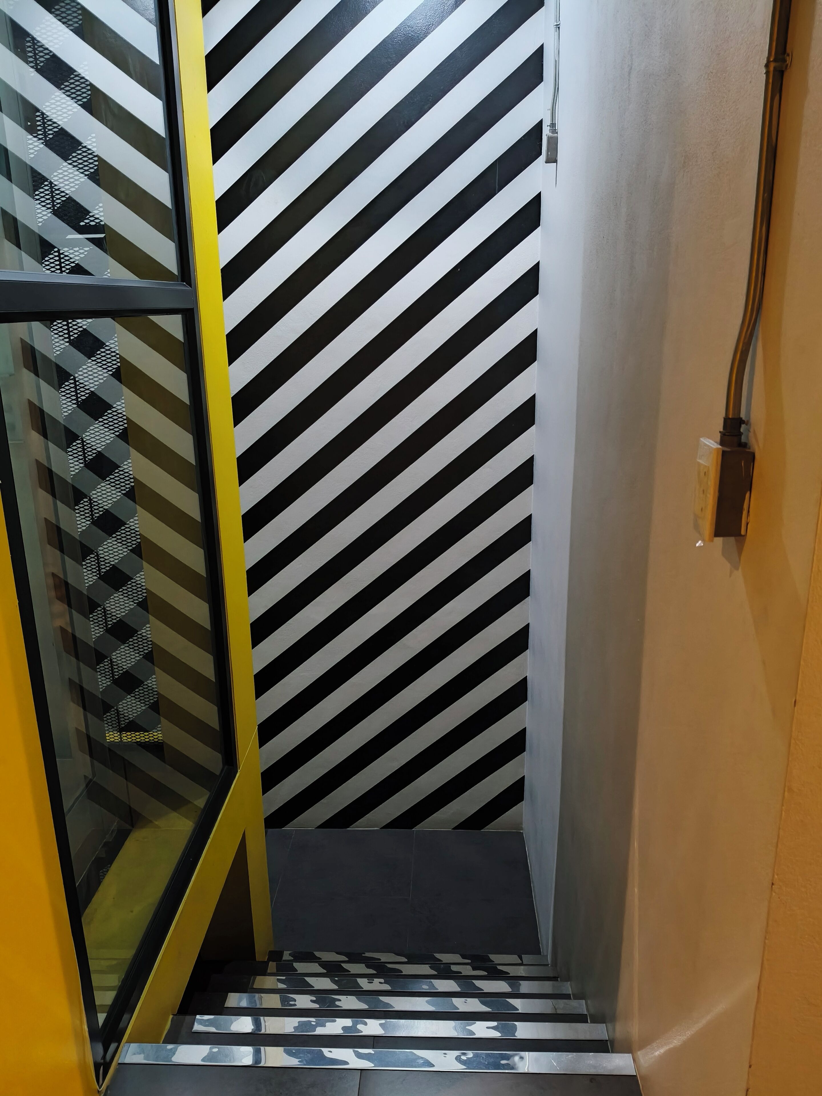 Een trap met zwart-wit diagonale strepen op de muren en een glazen deur met een geometrisch patroon.