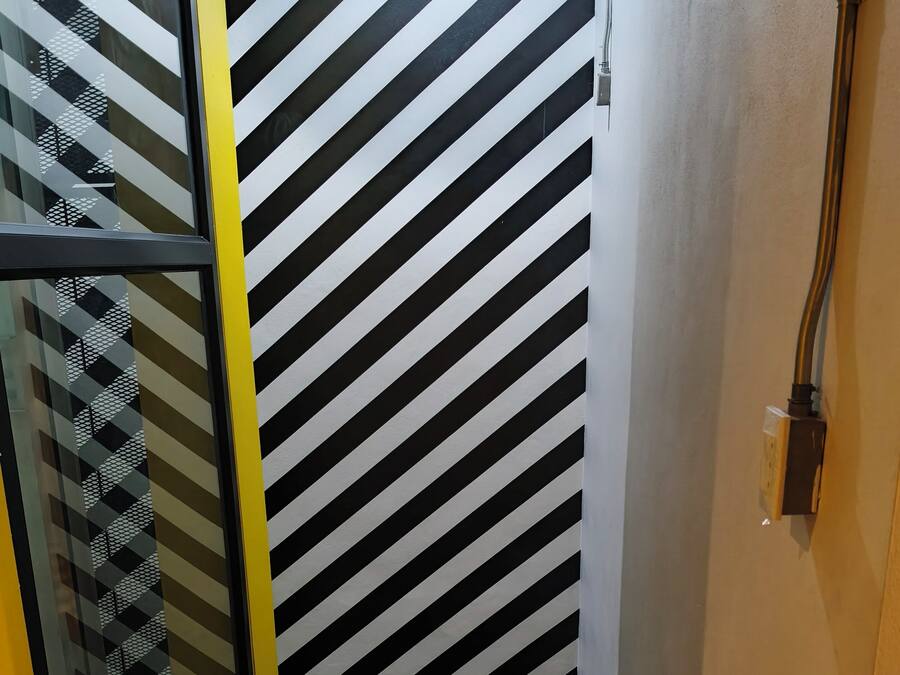Een trap met zwart-wit diagonale strepen op de muren en een glazen deur met een geometrisch patroon.