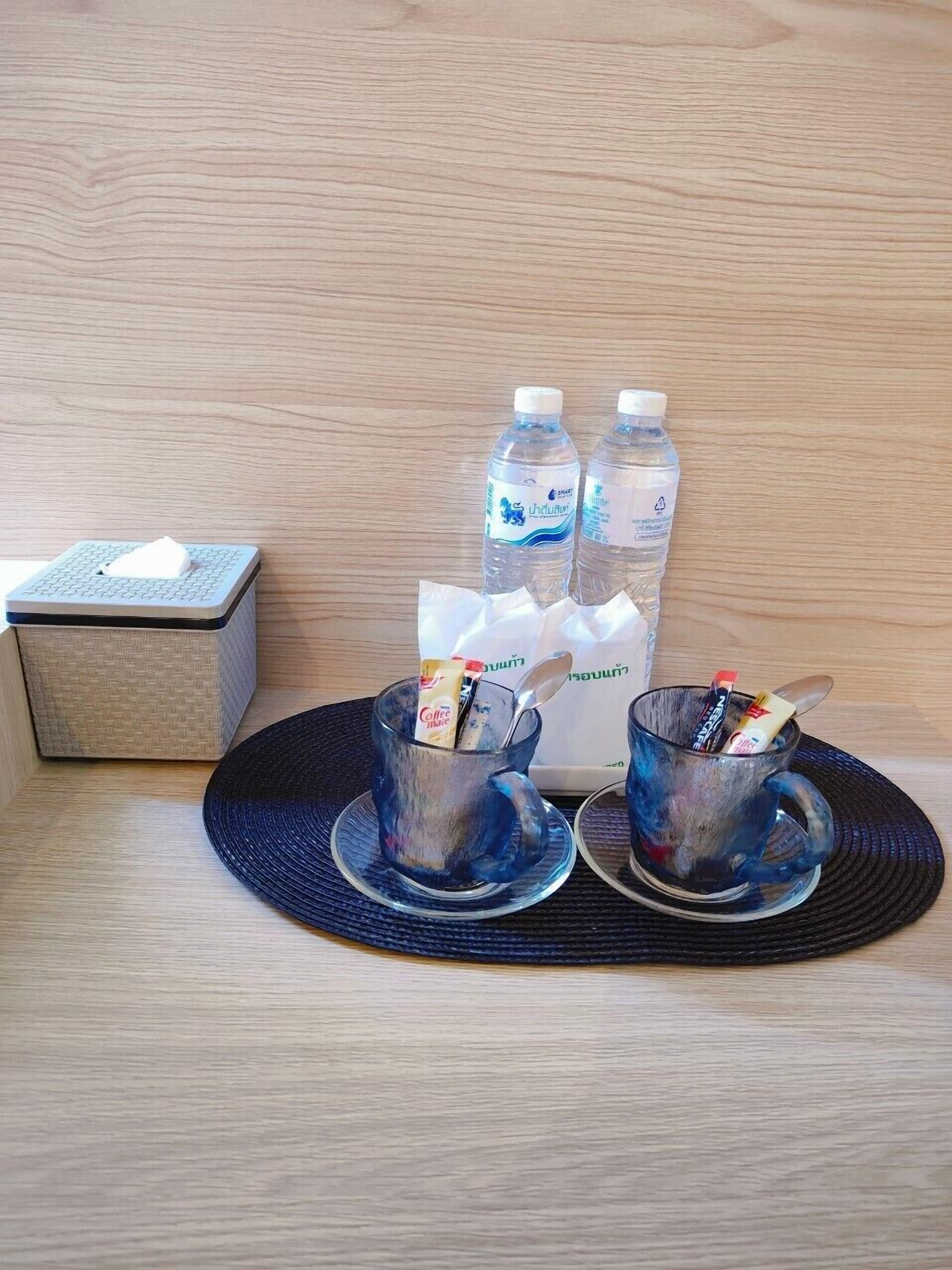 A table with two glasses containing coffee and sugar packets, two bottles of water, and a tissue box.