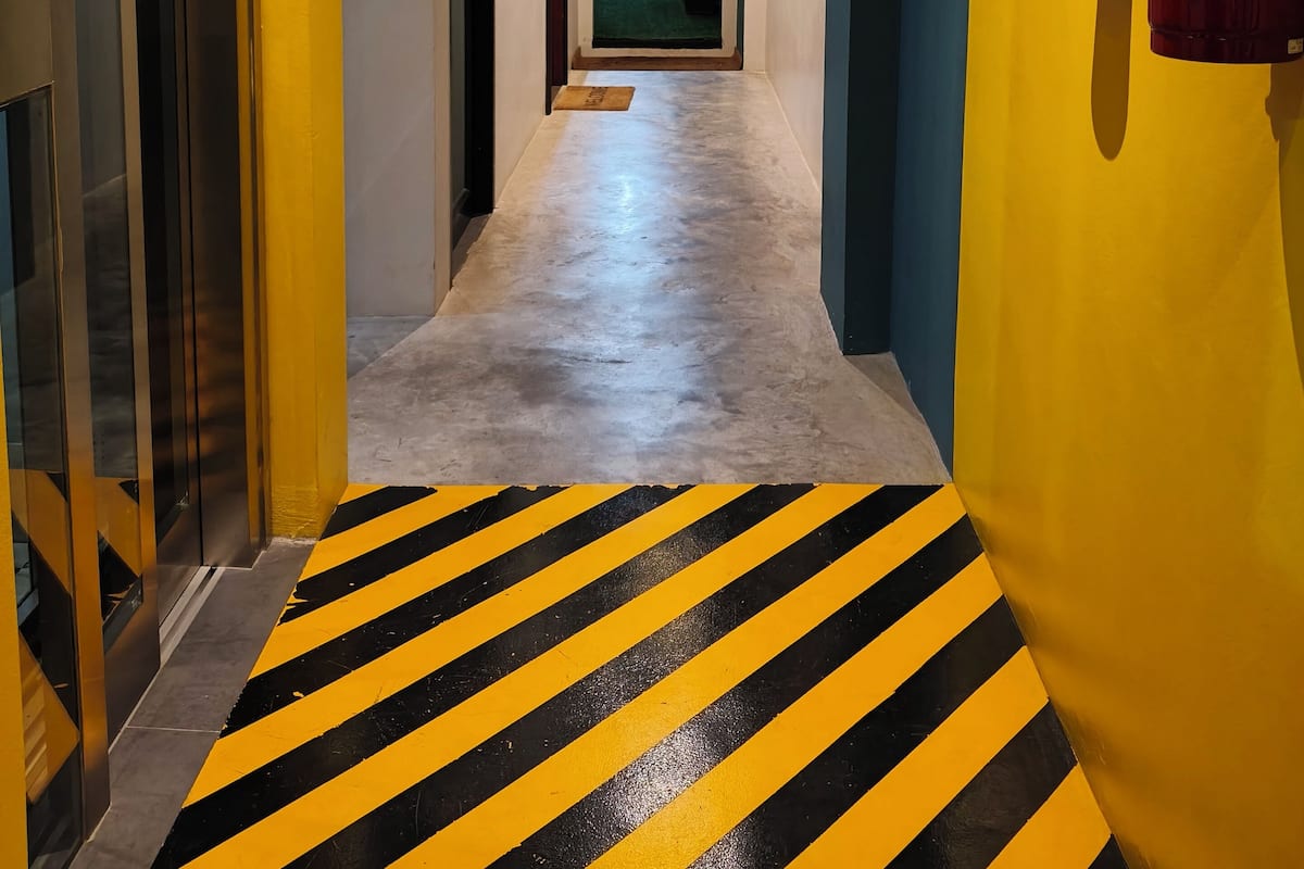 A hallway with a yellow wall, a fire extinguisher, and a striped floor.