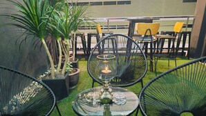 A seating area with black wireframe chairs, a glass table with a candle, and potted plants. - Icon Hotel Hatyai (Hat Yai)
