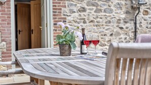 A wooden table with a potted plant and two wine glasses, set against a stone wall. - A charming property located in the quaint village of Holditch.  (Chard)