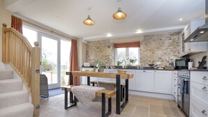 A modern kitchen with a stone wall, wooden table, and built-in appliances. - A charming property located in the quaint village of Holditch.  (Chard)