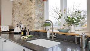 A kitchen with a stone wall, a sink, a window with a view, and various kitchen items on the counter. - A charming property located in the quaint village of Holditch.  (Chard)