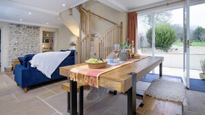 A cozy living room with a blue sofa, a wooden dining table with a bowl of fruit, and a staircase leading to a balcony. - A charming property located in the quaint village of Holditch.  (Chard)