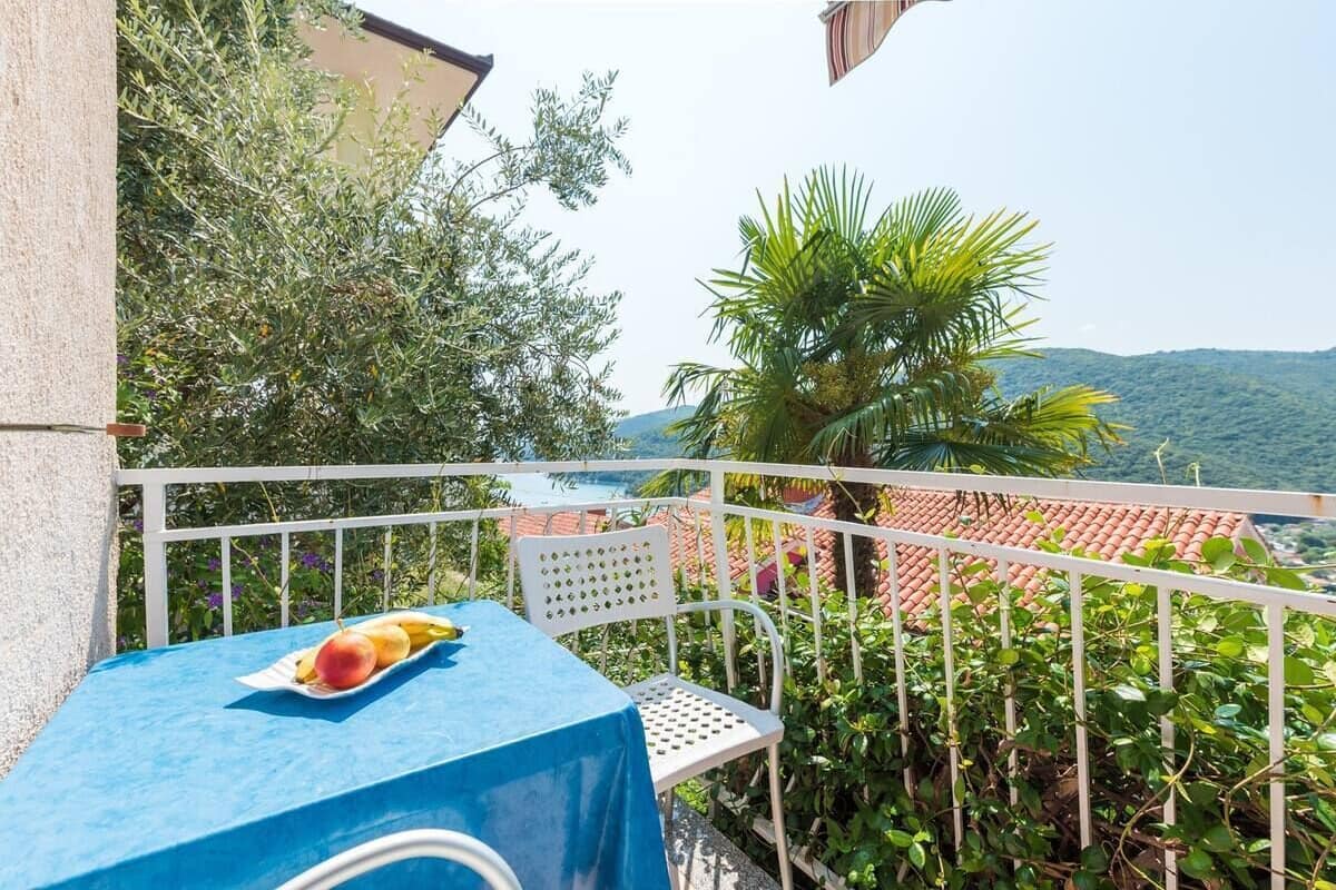 Un balcón con una mesa cubierta por un mantel azul, una silla y un plato con fruta.