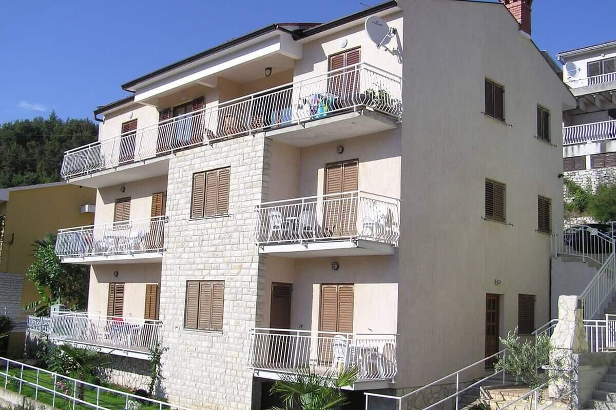 Un edificio residencial de varios pisos con balcones, fachada de piedra y una escalera que conduce a la entrada.