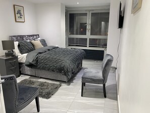 Ein Schlafzimmer mit einem Bett, einem Sessel, einem Nachttisch und einem Fenster mit Jalousien.