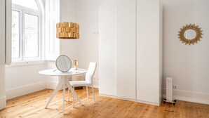 Una stanza con un tavolo bianco rotondo, una sedia, uno specchio, una lampada a parete e un termosifone.