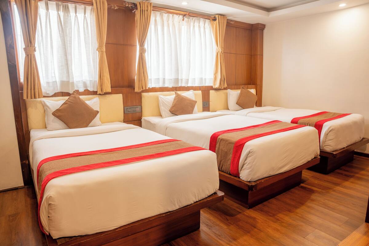 Quarto de hotel com três camas, cabeceiras de madeira e chão de madeira.