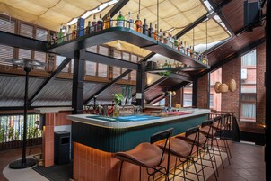 Zona de bar con techo alto, paredes de ladrillo visto y una variedad de botellas en estanterías.