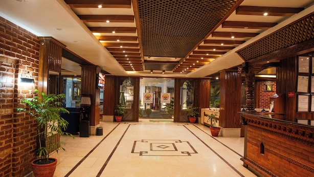 A hotel lobby with a brick wall, wooden reception desk, potted plants, and a patterned floor. - Hotel Kailash Kutee (Kathmandu)