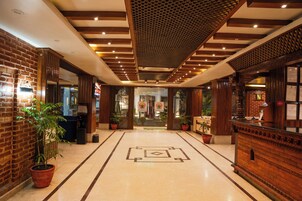 Un vestíbulo de hotel con pared de ladrillo, mostrador de recepción de madera, plantas en macetas y suelo estampado.