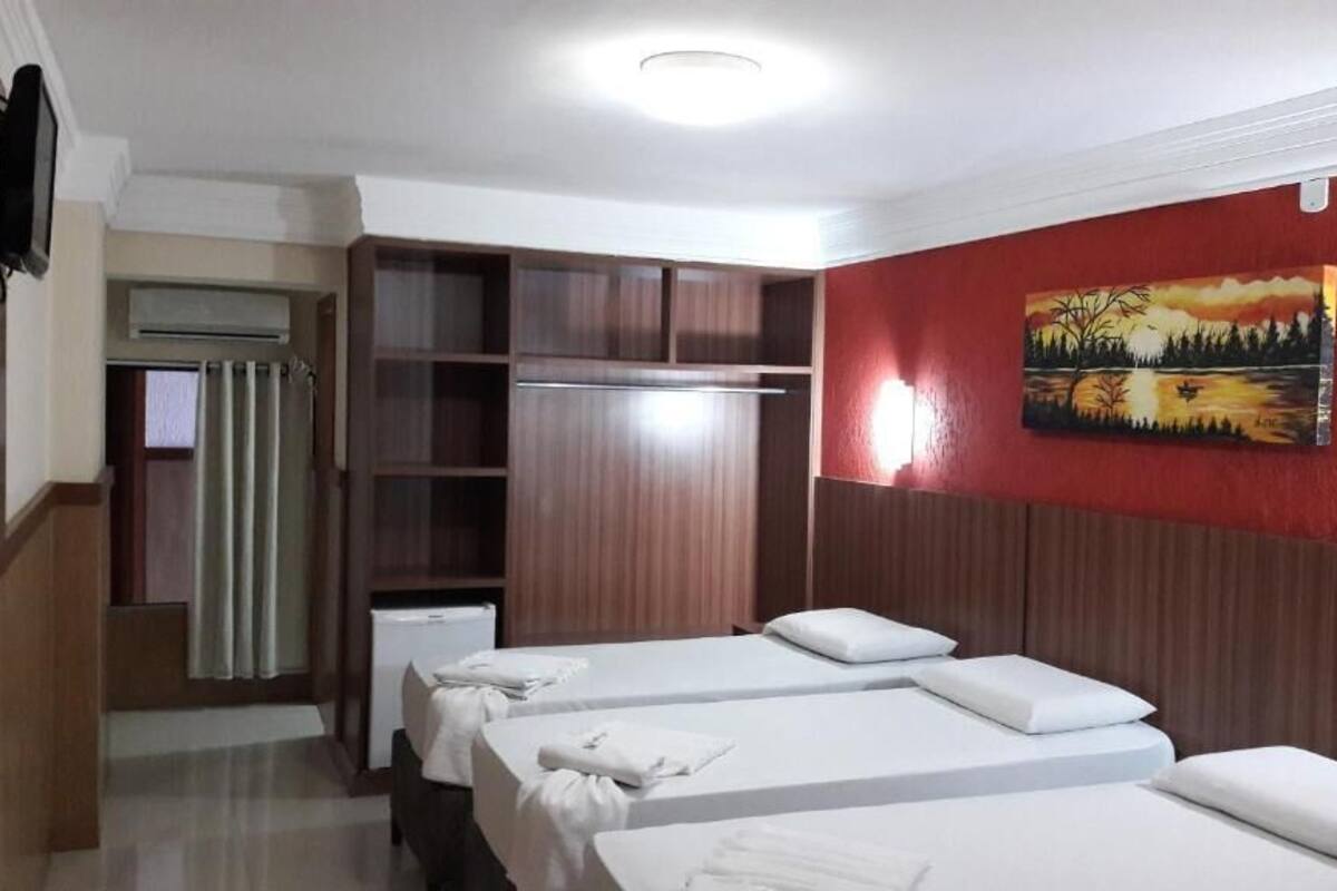 Ein Hotelzimmer mit drei Betten, einem Kleiderschrank und einem Gemälde an der Wand.