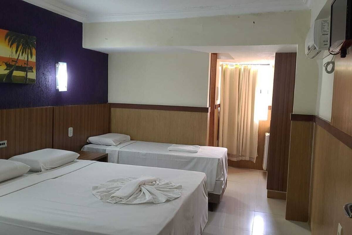 Ein Hotelzimmer mit zwei Betten, einem Bild an der Wand, einem Fenster und einer Tür zu einem anderen Raum.