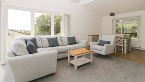 A spacious living room with a grey sofa set, a wooden coffee table, and a dining area with a table and chairs. - Harcombe House Bungalow 2 (Newton Abbot)