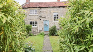 Une maison en pierre avec un toit recouvert de tuiles rouges, une porte bleue et un étroit sentier de pierre menant à l’entrée.