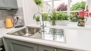 Une cuisine avec un évier en acier inoxydable, une bouilloire jaune et diverses plantes en pot disposées sur le rebord de la fenêtre.