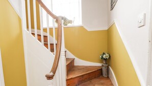 Un escalier avec des marches en bois et des rampes blanches, menant à un palier où se trouve un vase de fleurs.