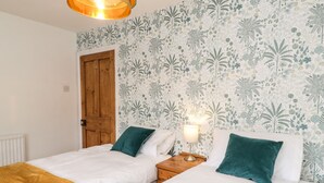 Une chambre avec deux lits, une porte en bois, un radiateur et un mur orné d’un motif floral.