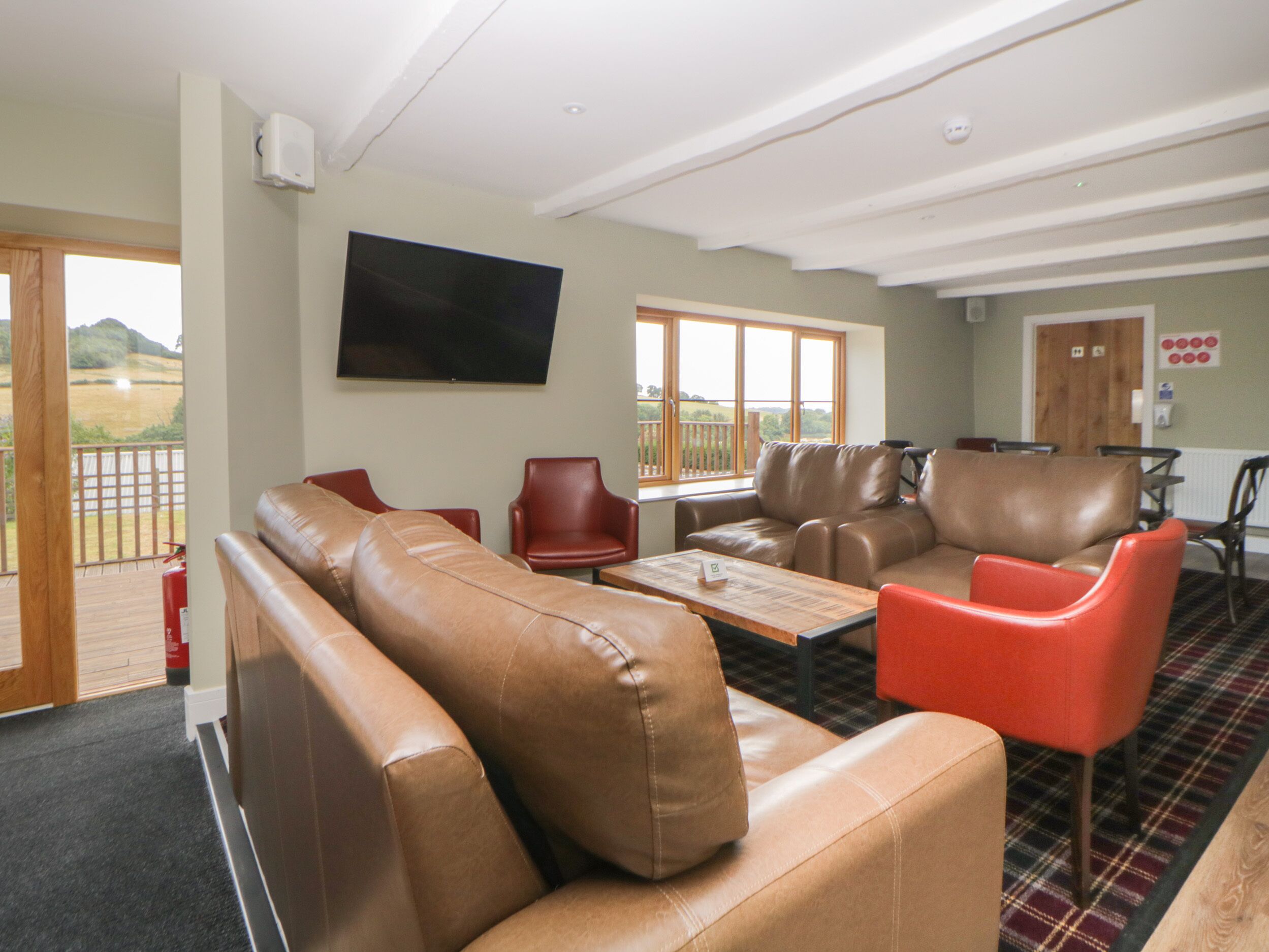 A spacious living area with leather sofas and armchairs, a flat-screen TV mounted on the wall, and a view of the outdoors through large windows.