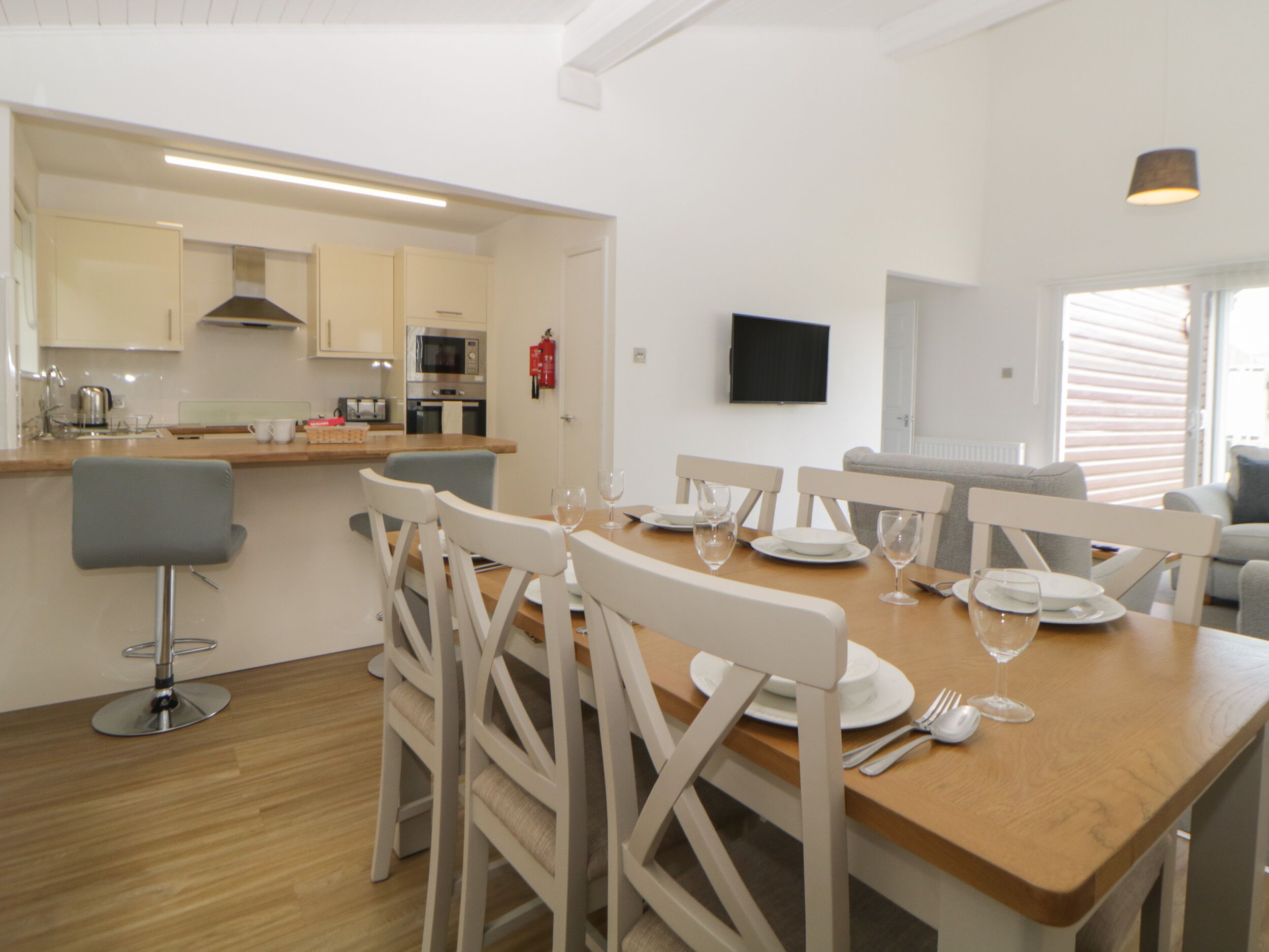 Cocina moderna con armarios blancos, un microondas y una estufa. Hay una zona de comedor con una mesa de madera y sillas blancas.