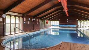 Piscina interna com vigas de madeira, prancha de mergulho e placas de segurança.