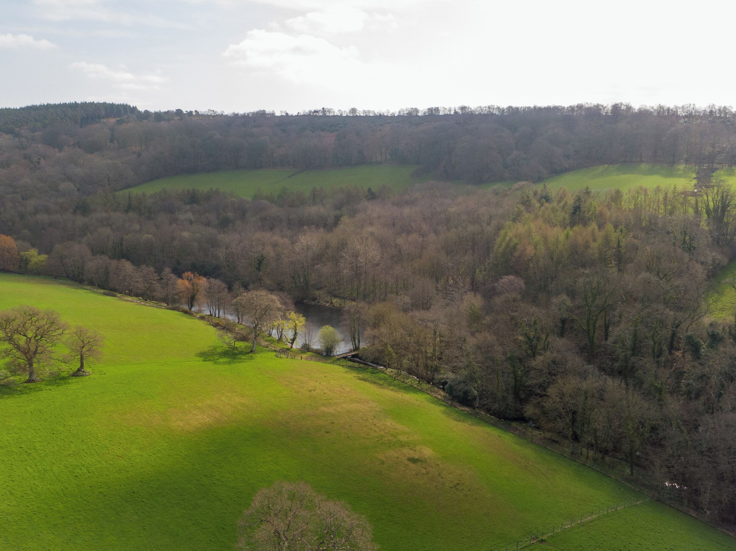 A rural landscape with rolling hills, a river, and a bridge.
