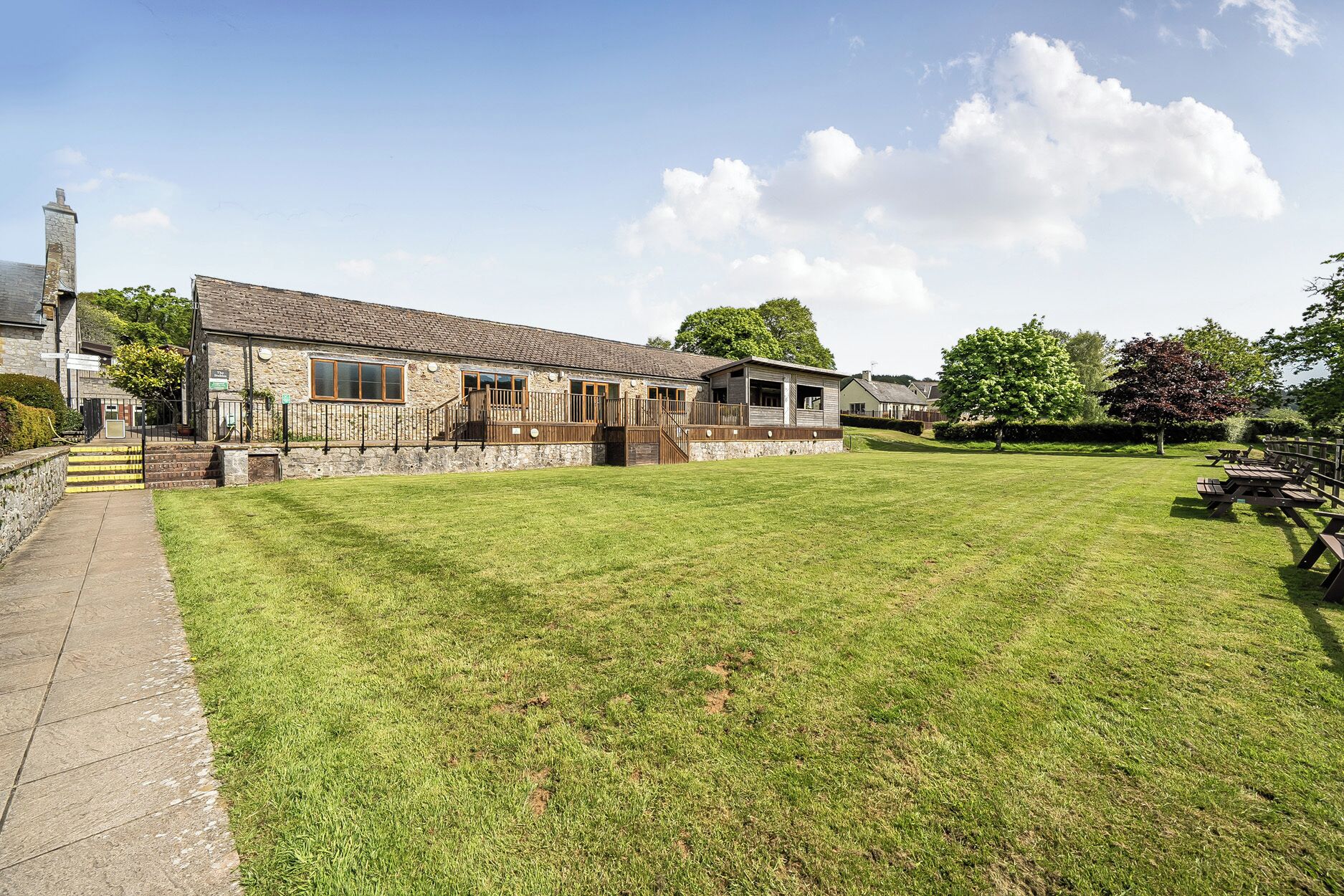 A stone building with a large lawn, a wooden deck, and a staircase leading to the entrance.