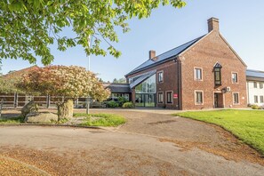 A brick building with a modern glass entrance, a stone pathway, and a tree in the foreground. - Jubilee Three Bedroom House Pet Free (Penrith)