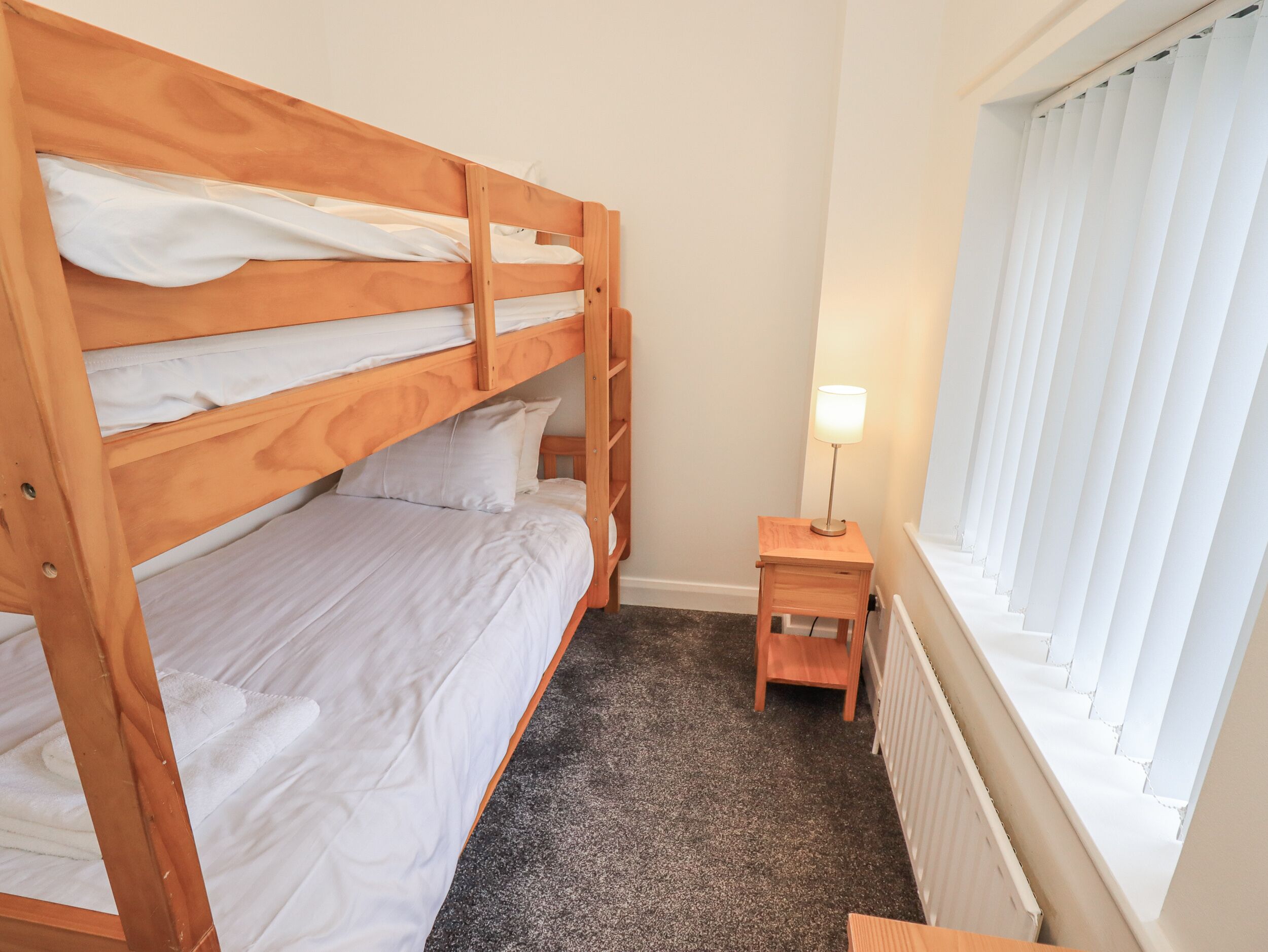 A bunk bed room with a small wooden nightstand and a lamp.