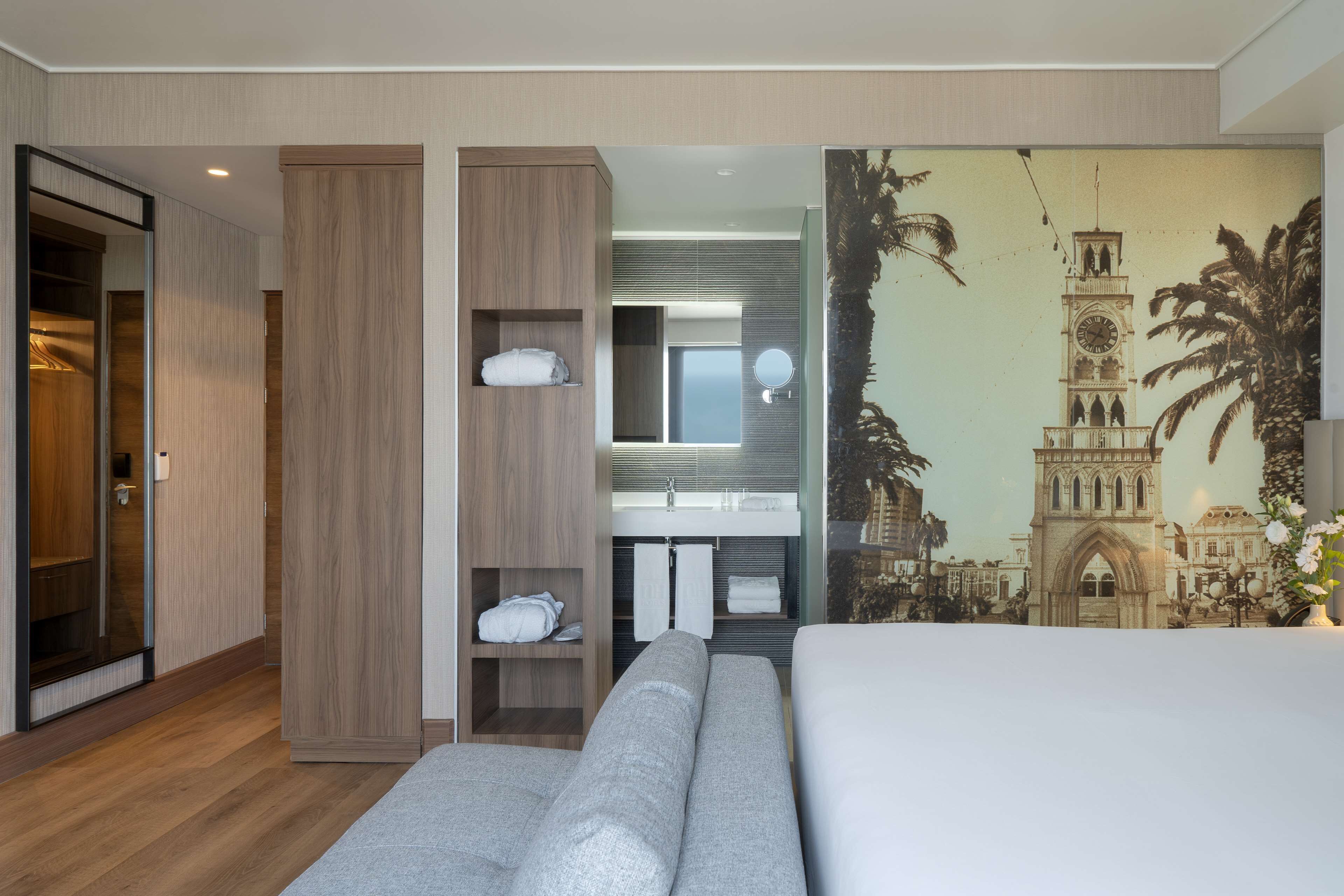 Habitación de hotel con una cama grande, un armario, una tocador con espejo y un mural de un edificio histórico.