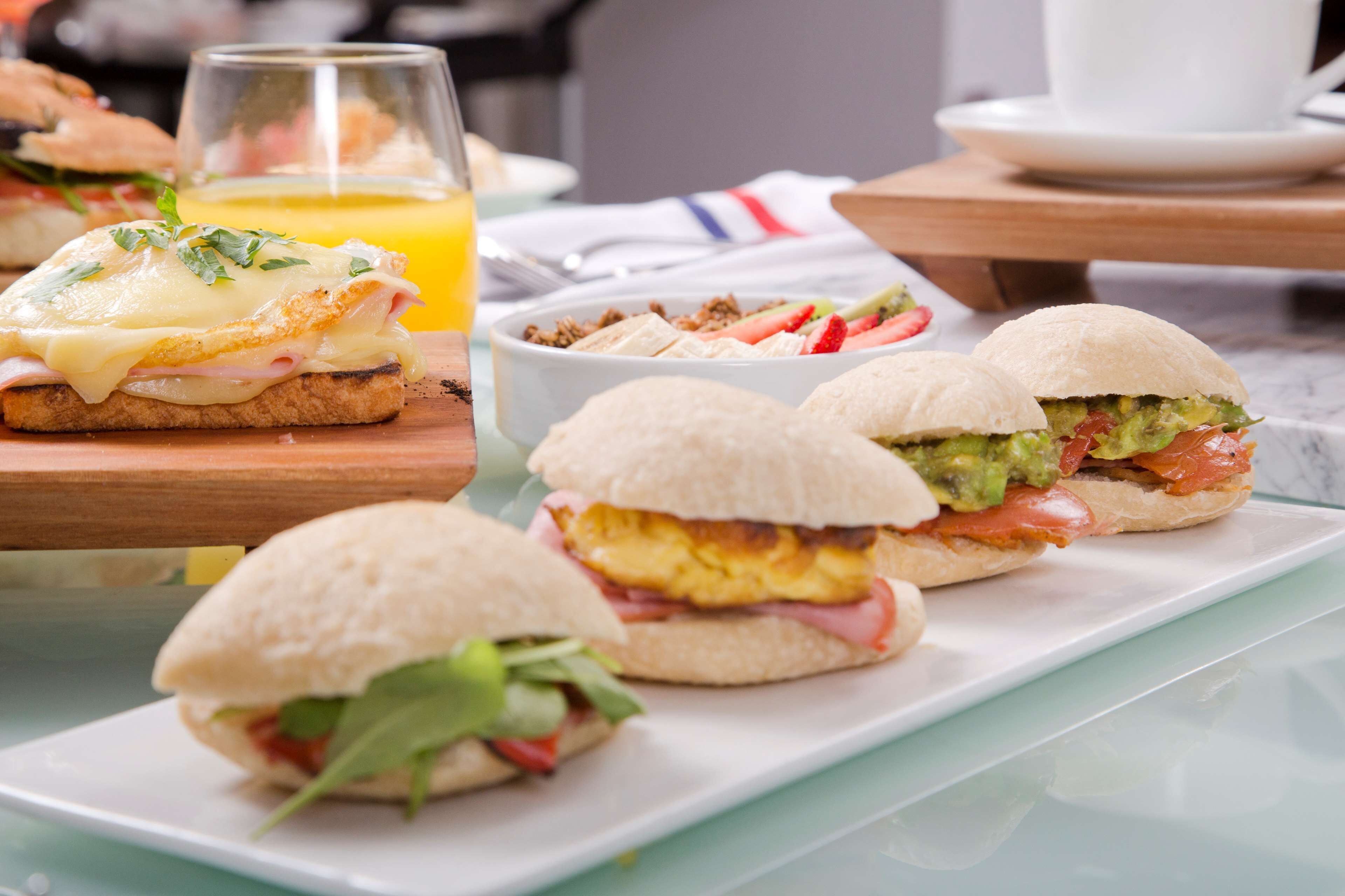 A breakfast setting with sandwiches, a glass of orange juice, and a white cup on a table.