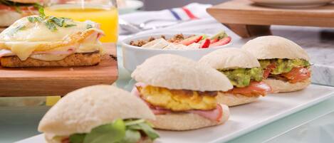 A breakfast setting with sandwiches, a glass of orange juice, and a white cup on a table.