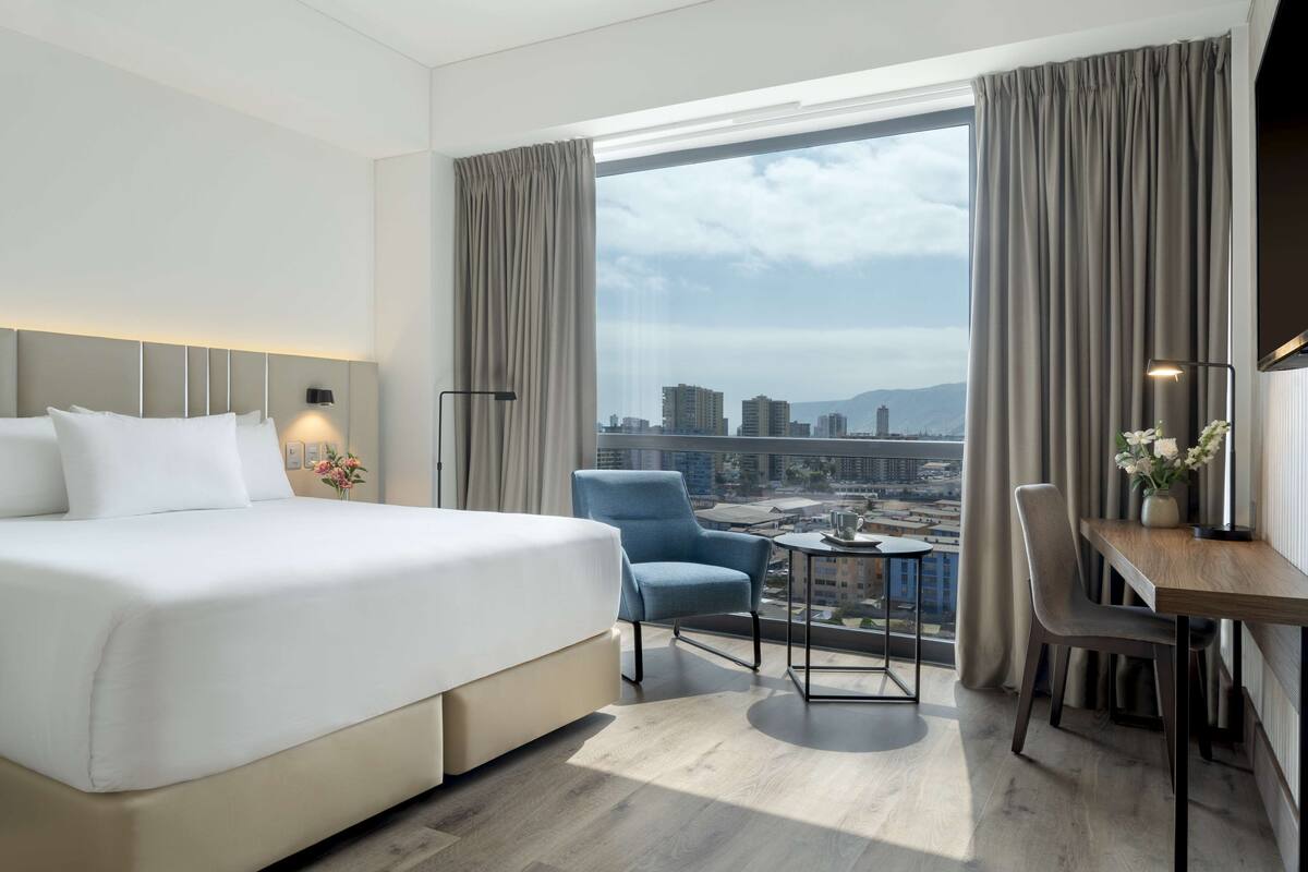 Een moderne hotelkamer met een groot bed, een bureau en een uitzicht op de stadslijn door een groot raam.