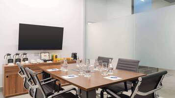 A conference room with a large table, chairs, a TV, and various amenities like coffee makers and water bottles.