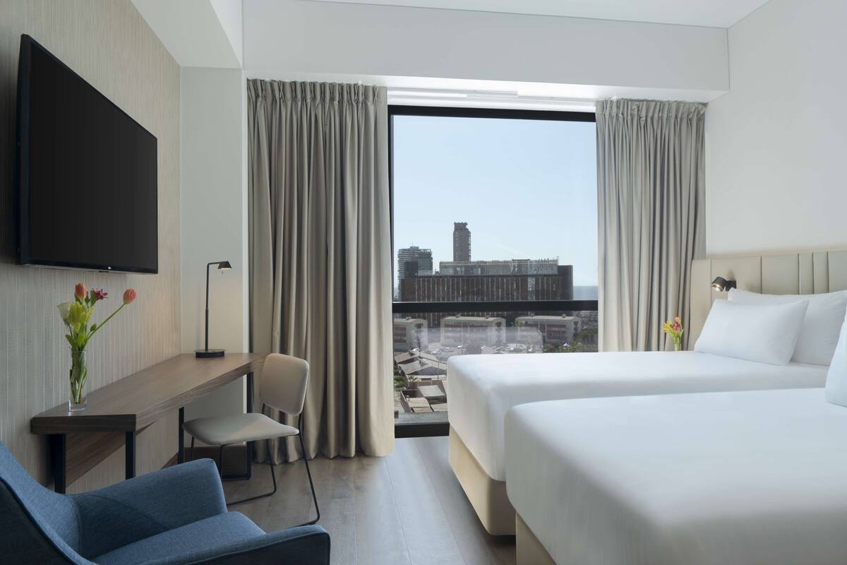 Een hotelkamer met een bed, een bureau, een stoel, een televisie en een groot raam met gordijnen.