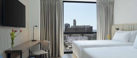 A hotel room with a bed, a desk, a chair, a TV, and a large window with curtains.