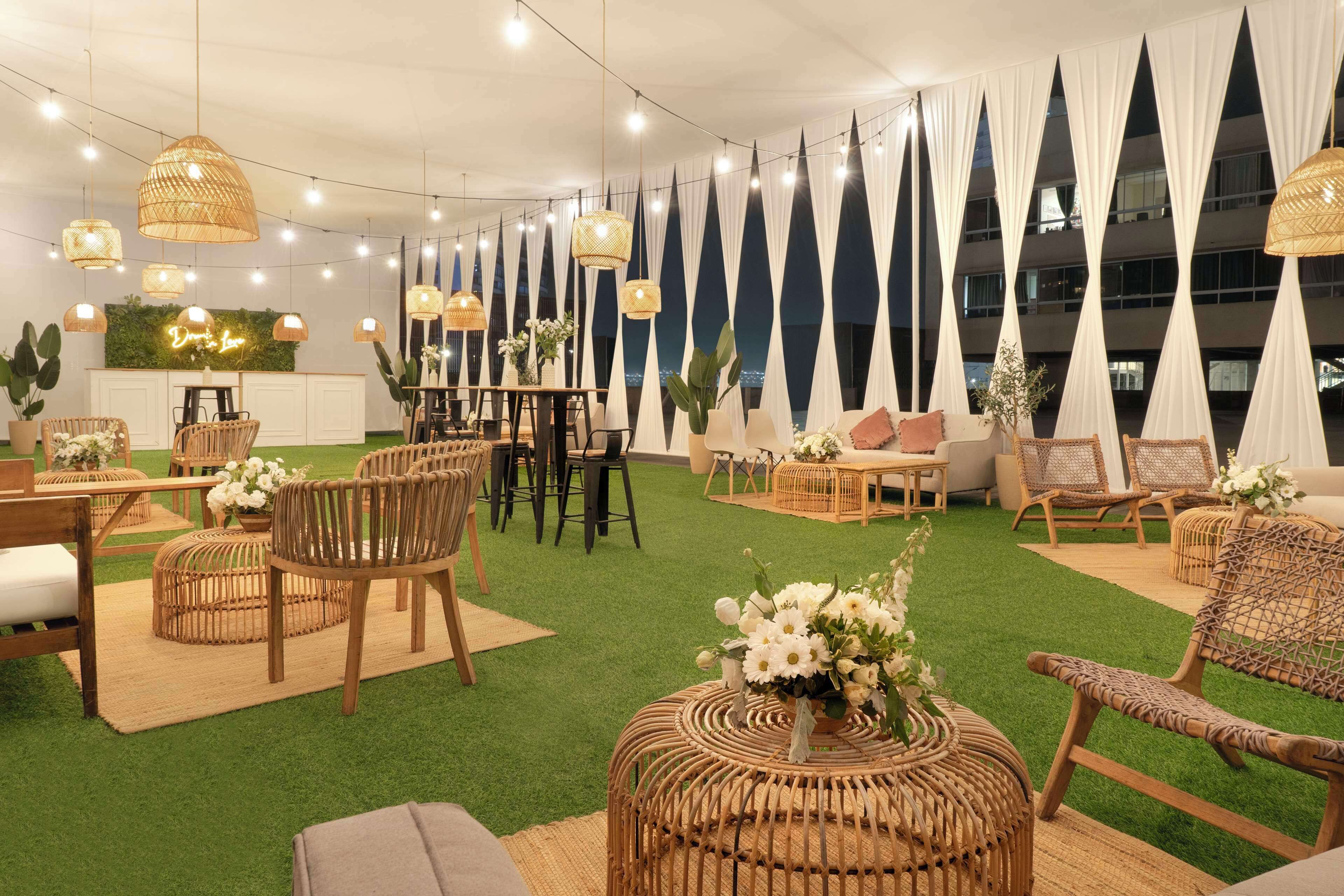 An outdoor seating area with wicker furniture, string lights, and a view of the city at night.