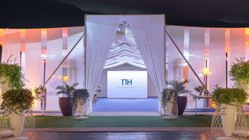 A hotel entrance with a modern design, featuring a large digital display, white drapes, and potted plants.