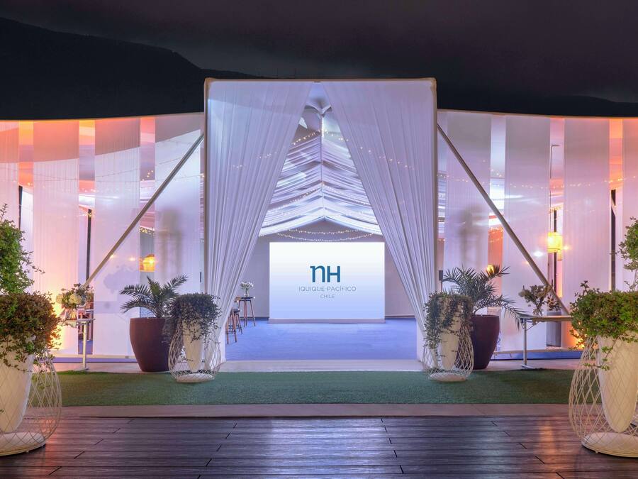 A hotel entrance with a modern design, featuring a large digital display, white drapes, and potted plants.