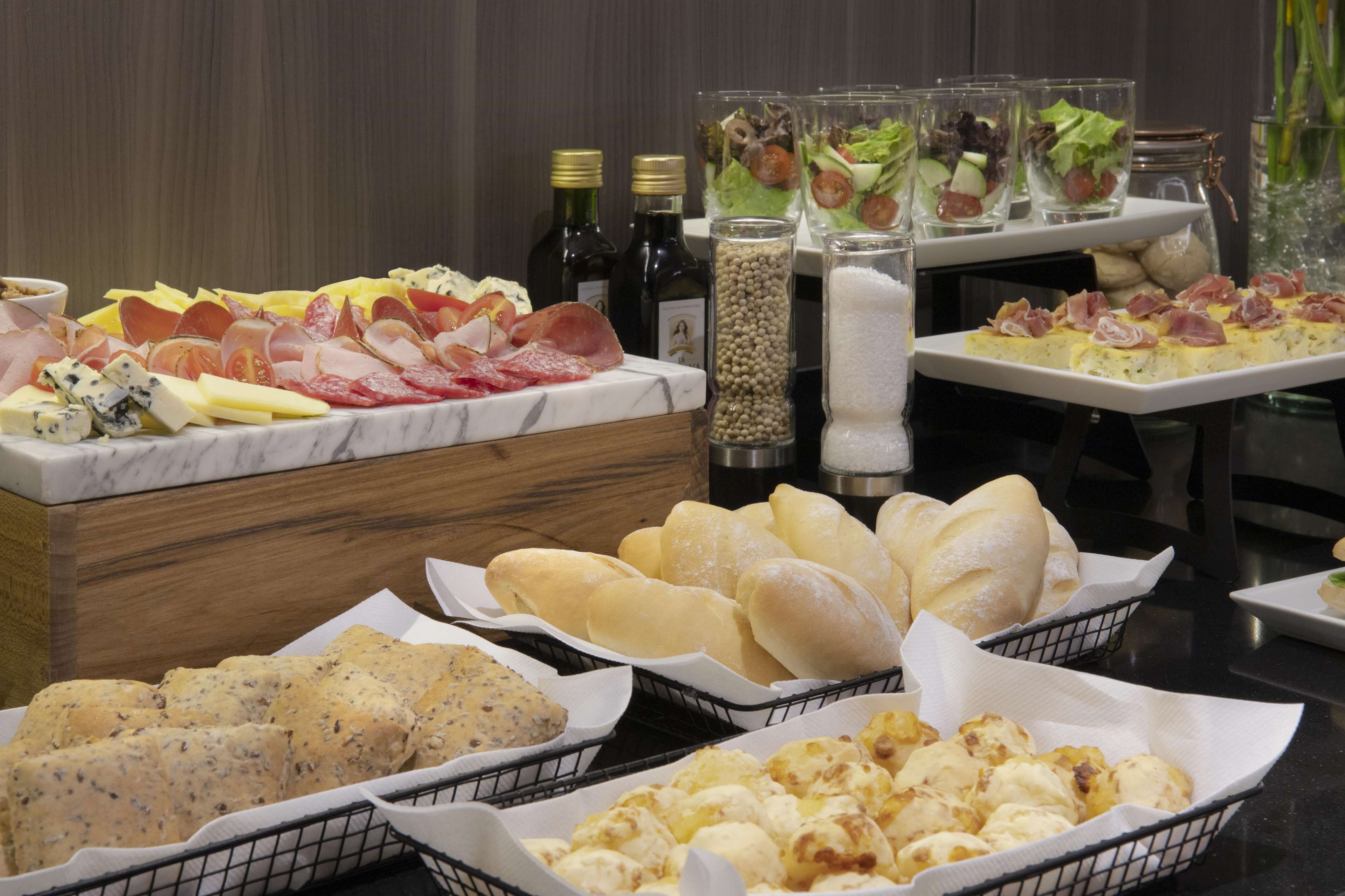 A buffet with various cheeses, meats, breads, and salads.