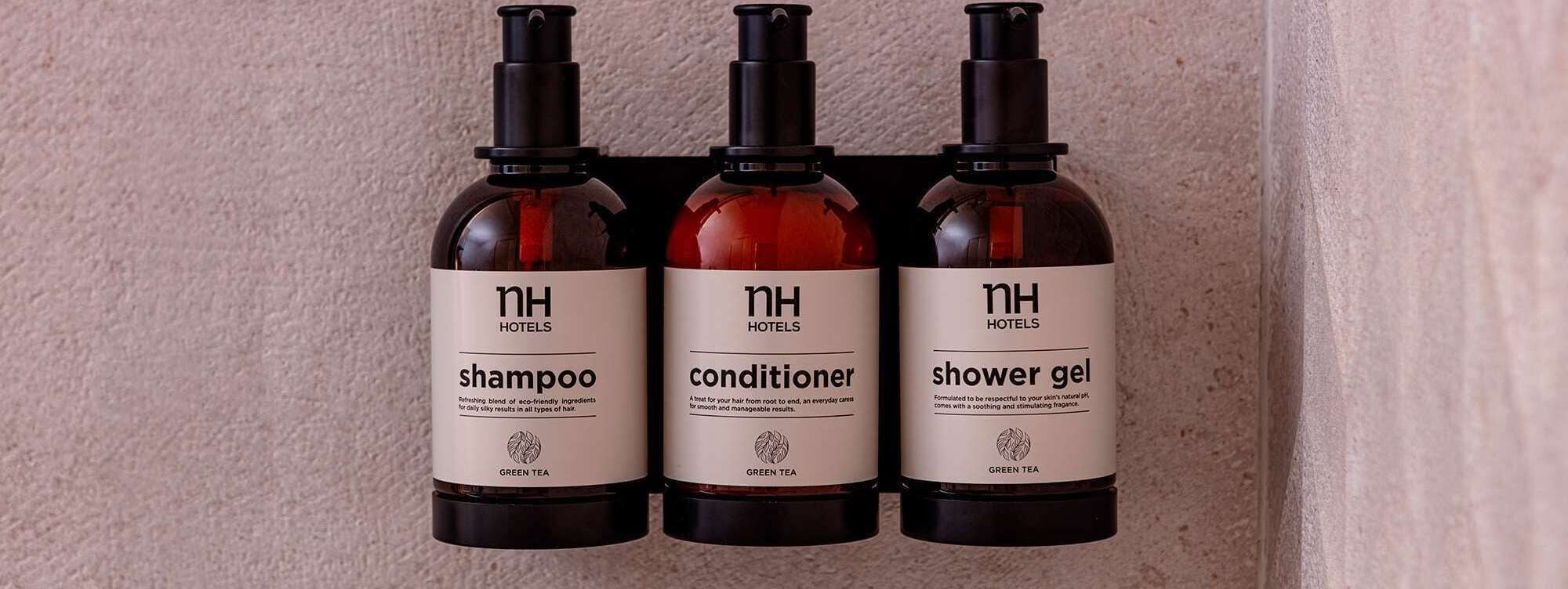 Three bottles of NH Hotels products: shampoo, conditioner, and shower gel.