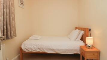 A neatly made bed with white linens and pillows, a bedside lamp, and a small wooden nightstand.