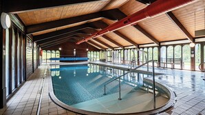 Une piscine intérieure dotée d’un plafond en bois et de grandes fenêtres.