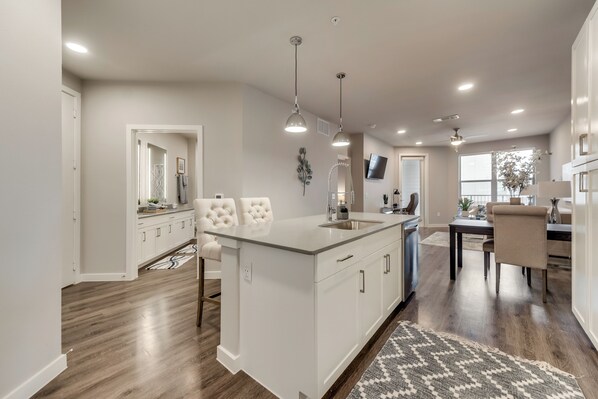 A modern kitchen with a central island, white cabinetry, and a dining area with a table and chairs.
