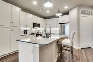 A modern kitchen with white cabinetry, stainless steel appliances, and a central island with bar stools.