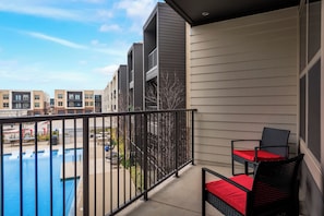 A balcony with a pool, outdoor seating, and a view of neighboring buildings.