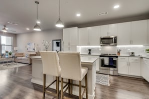 Une cuisine moderne avec des meubles blancs, des appareils en acier inoxydable et un îlot central doté de tabourets de bar.